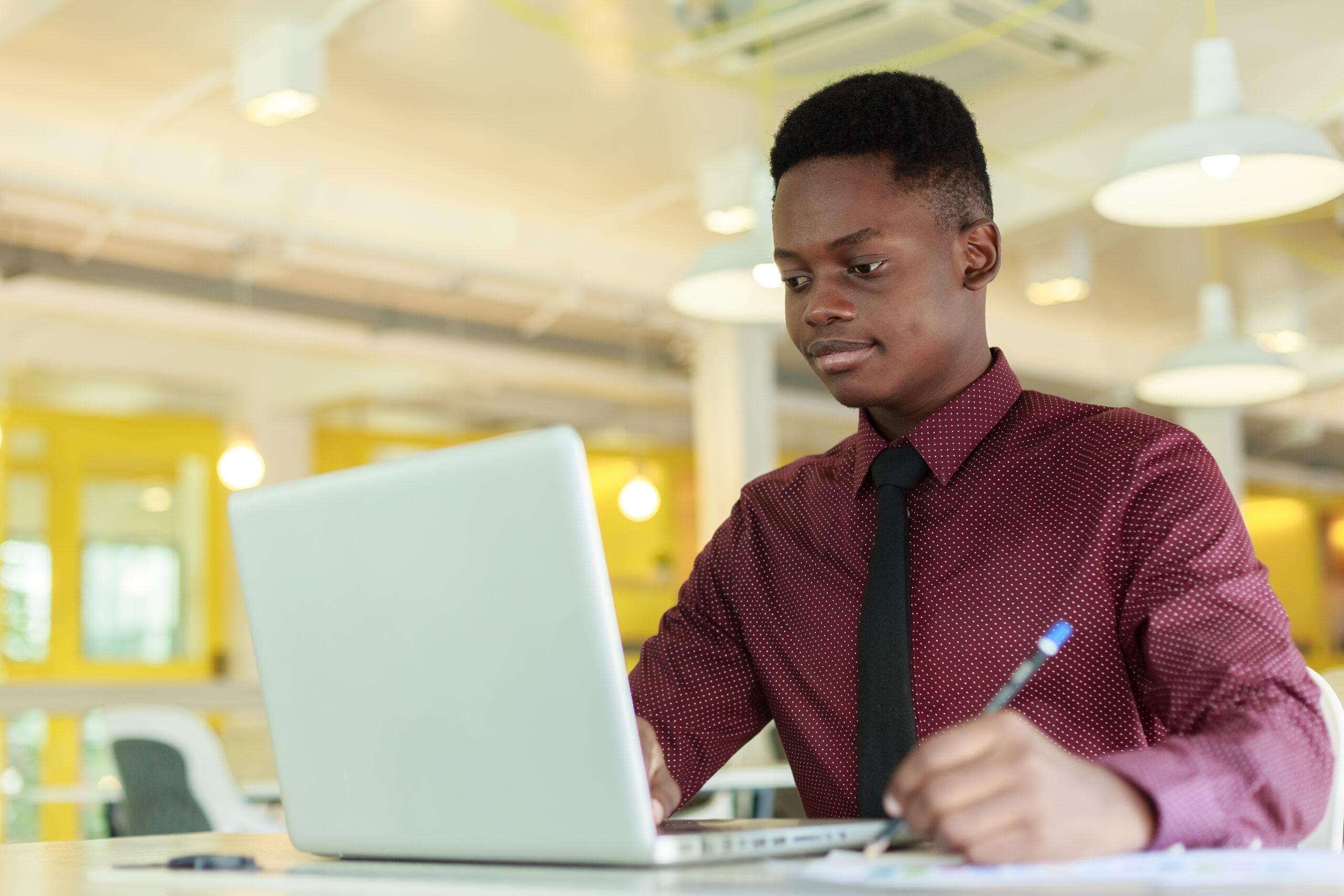 A young professional using a laptop while writing on a notebook